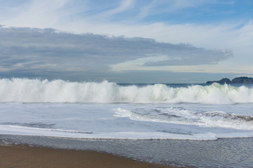 Sandy seashore and white waves under sky