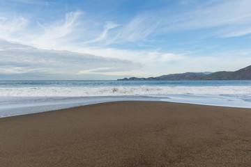 Sandy seashore and white waves under sky