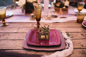Romantic dinner of the bride and groom on a wooden table with burgundy plates and fresh flowers. 