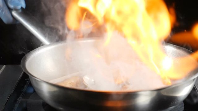Unrecognizable cook tossing hot non-stick frying pan with seafood , then setting it on fire cooking flambe dish. Slow motion foodvideo footage. hd