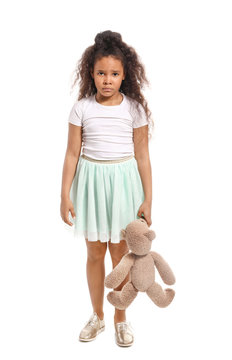 Sad African-American girl with toy bear on white background