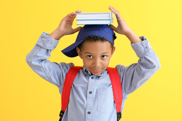 Cute African-American schoolboy on color background