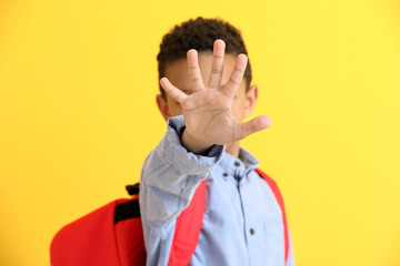 Cute African-American schoolboy showing STOP gesture on color background
