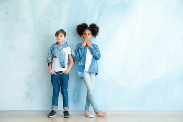 Stylish children in jeans clothes near color wall