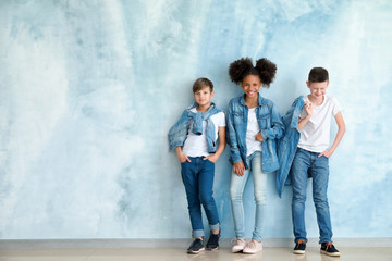 Stylish children in jeans clothes near color wall