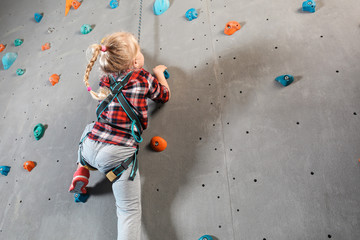Fototapeta premium Little girl climbing wall in gym