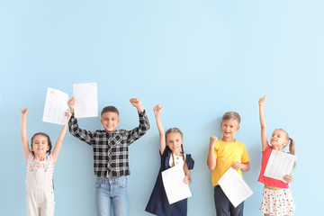 Happy children with answer sheets for school test on light color background