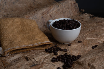 Coffee beans are in a white cup with a sack placed near, top view coffee cup for background,Concept:ingredient mocha breakfast drink food fresh