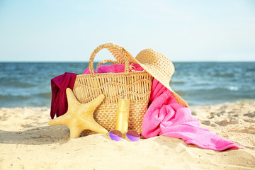 Fototapeta na wymiar Bag with starfish, swimsuit, hat, sunglasses and cosmetics on sand beach
