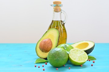 Concept of healthy food with cut avocado, limes and a bottle of olive oil on blue and white background.