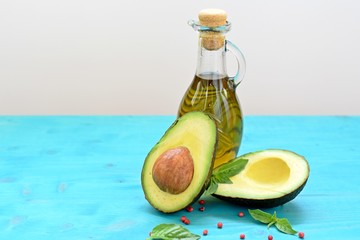 Concept of healthy food with cut avocado and a bottle of olive oil on blue and white background.