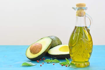 Concept of healthy food with cut avocado and a bottle of olive oil on blue and white background.