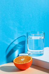 On a yellow-blue background, a glass with water, lemon and orange. Fresh summer still life with water and tropical fruits