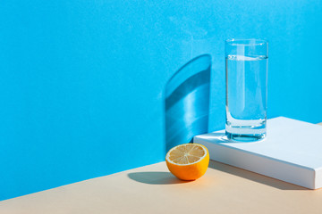 On a yellow-blue background, a glass with water, lemon and orange. Fresh summer still life with water and tropical fruits