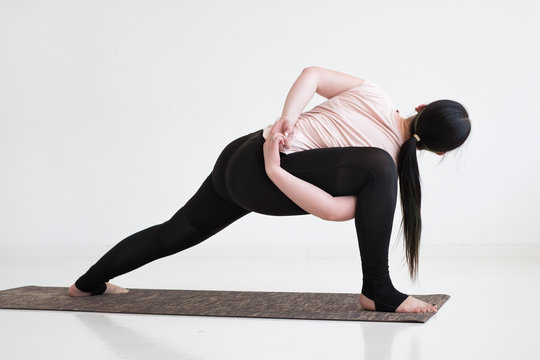 Woman practicing yoga, standing in Revolved Bound Side Angle exercise, Parivrtta Parsvakonasana pose, working out. Indoor full length, rear view