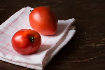 Two fresh large red tomatoes on kitchen towel, on brown background.