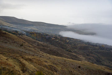 Mountains shrouded in mist in the season of golden autumn on a cloudy day, view of the ancient village in the gorge from the top of the mountain.
