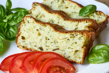 Casserole with zucchini, cheese and fresh herbs on a white plate