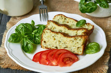 Casserole with zucchini, cheese and fresh herbs on a white plate