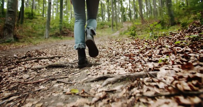 Woman in trekking boots and blue jeans walking in forest, lowangle view in footwear