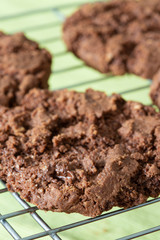 Homemade chocolate cookies biscuits, with chocolate chips, on a metal cooling rack, with a green tablecloth underneath