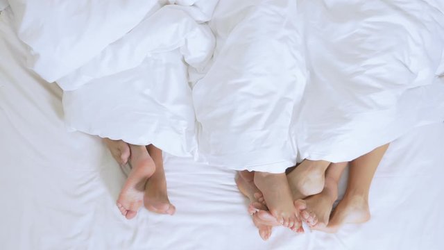 Concept Sex clubs, swing clubs, lifestyle clubs, formal, informal groups. feet of a group of people under a white blanket on a white sheet on a king size bed