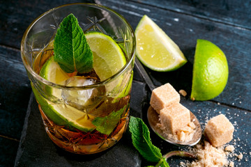 Whiskey and Cola cocktail with lime, mint, brown sugar and ice, alcoholic drink in a glass on a...