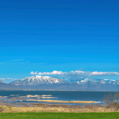 Grassy terrain with view of lake and snowy mountain under blue sky on sunny day