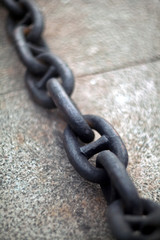 An old heavy iron chain from a sea anchor lying on a pier concrete slab with blurred background.