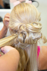 woman hairdresser making hairstyle to blonde girl bride in beauty salon