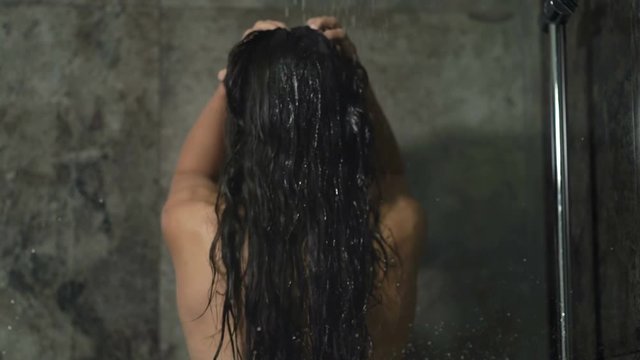 Young woman showering and washing hair in the bathroom. View from back.