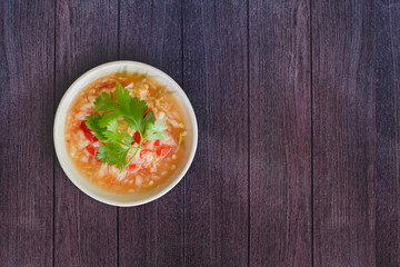 Top view Thai seafood dipping sauce in white bowl. Make from garlic, red chili, fish sauce, salt, sugar, lime juice and coriander topping on dark wooden texture for background. Copy space.
