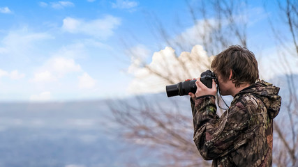 Panorama Side view of a man holding a camera with tree and cloudy blue sky background