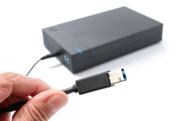 Hand holding USB plug, cable for external hard drive casing isolated on white background.