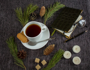 Cup of fragrant hot tea among Christmas tree branches and pine cones on a plaid.