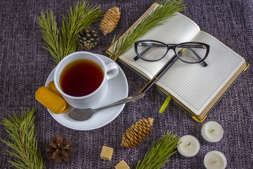 Cup of fragrant hot tea among Christmas tree branches and pine cones on a plaid.