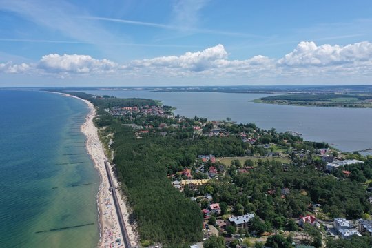 Drone Aerial Perspective View on Touristic City Located on narrow Spit between Sea and Lake with sunbathers on sand beach.