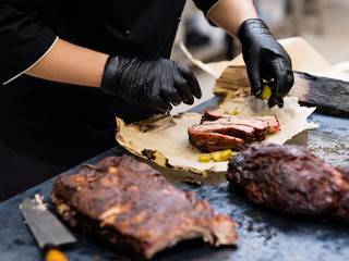 Grill restaurant kitchen. Cropped shot of chef in black cooking gloves serving smoked pork ribs. - obrazy, fototapety, plakaty