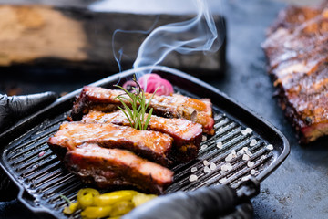 Culinary master class. Closeup of smoked pork ribs, served in griddle pan and decorated with...