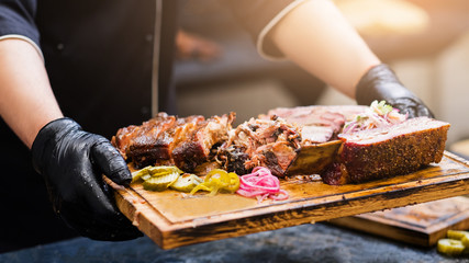 Professional catering. Cropped shot of chef holding wooden board with smoked meat assortment. - obrazy, fototapety, plakaty
