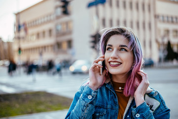 Stylish girl with dyed hair talking on a phone at city street.