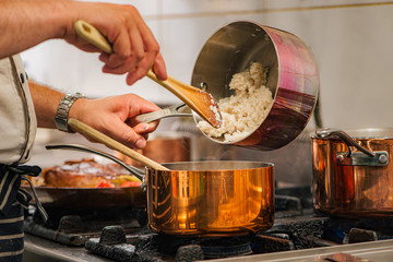 Chef pouring rice from one cooker to other on a stove, close-up.