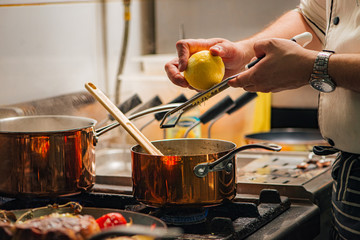 Professional chef grating lemon while preparing dish on a stove.