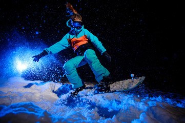 Active female snowboarder dressed in a orange and blue sportswear jumping on the mountain slope