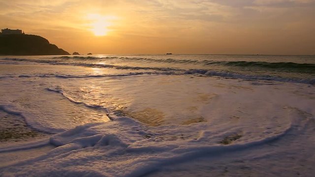 Sea waves washing onto sandy beach at sunset