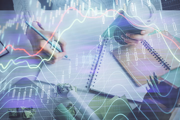 Financial forex graph displayed on hands taking notes background. Concept of research. Multi exposure