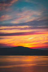 Naklejka na ściany i meble Beautiful burning cloudy sunset at the lake with sun gone behind the mountains