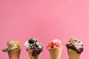 Various ice cream in waffle cones on a pink background.