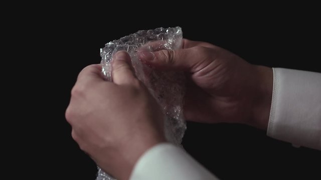 Male hands popping the bubbles in bubble wrap to relieve stress. Soothing therapy for nervousness or just for fun.