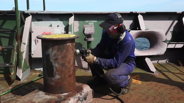 RIGA/LATVIA - JUNE 24 2019: specially equipped worker removes rust from vessel anchor stand with angle grinder on sailing ship deck on June 24 in Riga
